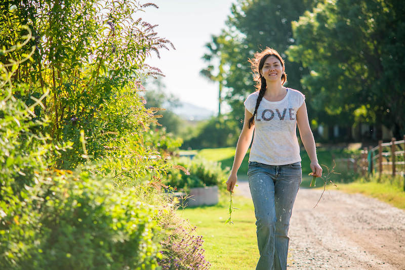 Young woman walking down a country road next to plants.